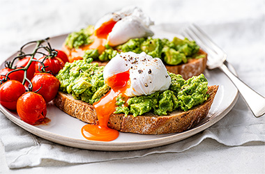 Smashed avocado on toast with poached eggs and tomatoes